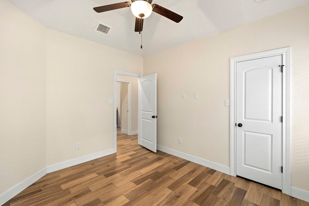 the spacious living room with a ceiling fan and wood flooring