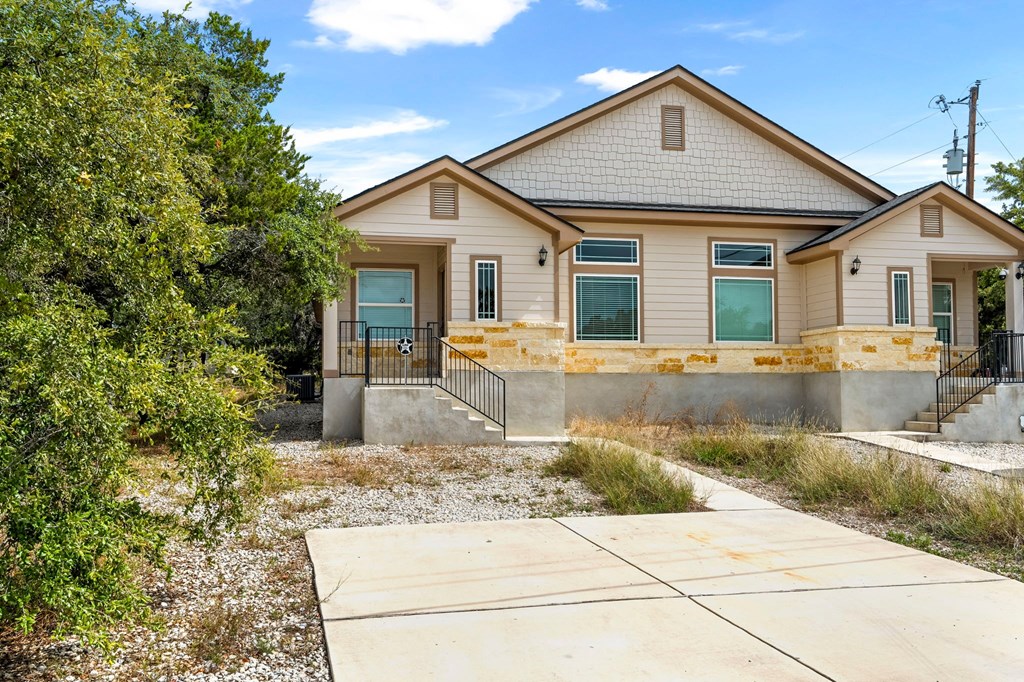 the front of a tan house with green doors and a driveway