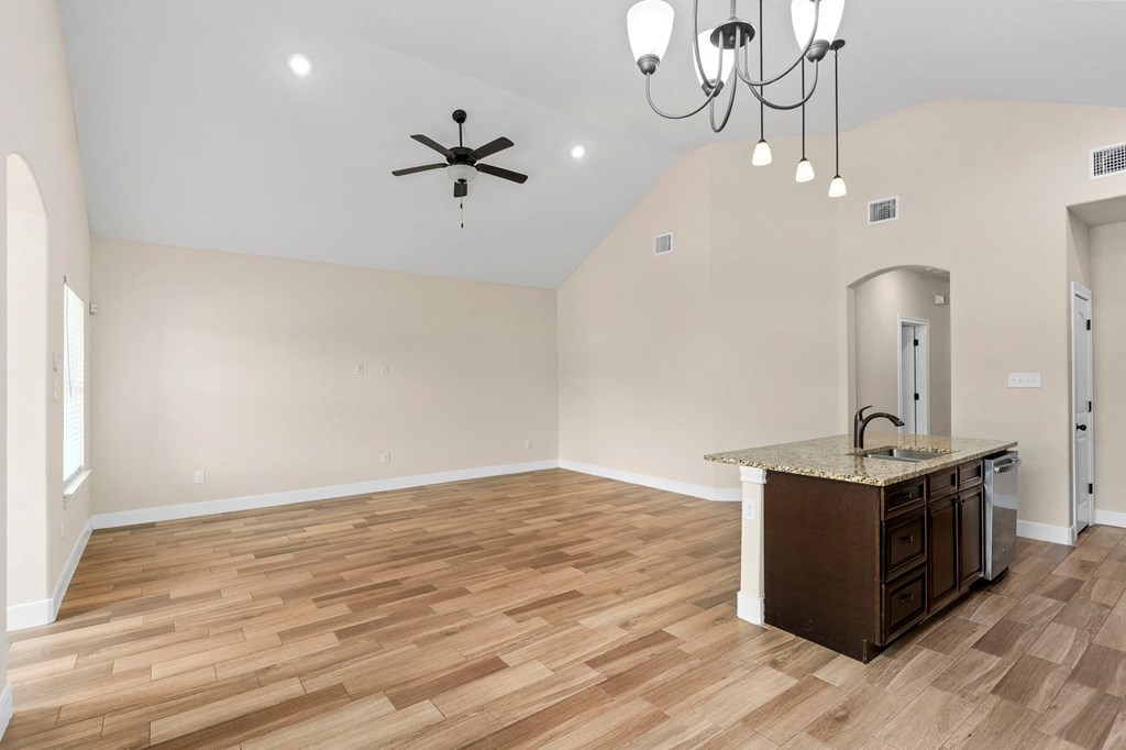 an empty living room with a kitchen and a ceiling fan