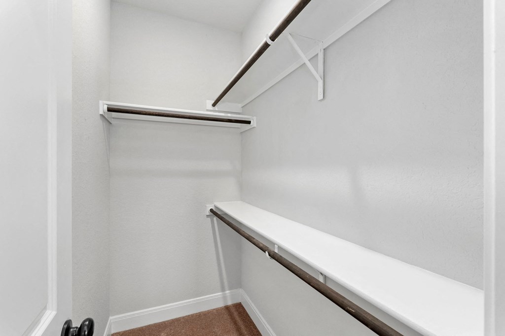 a walk in closet with white walls and a white bench