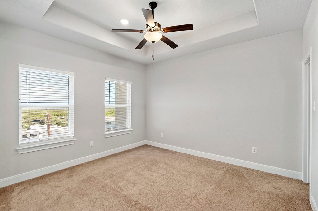 an empty living room with a ceiling fan and two windows