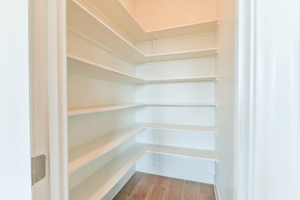 a walk in closet with white shelves and a wood floor
