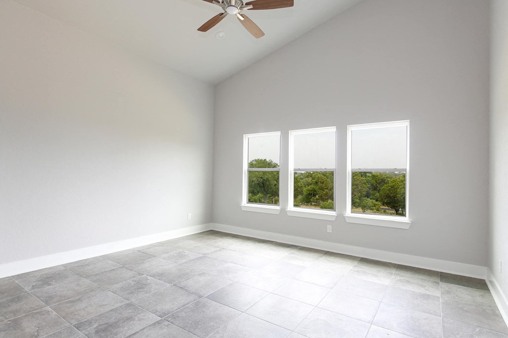 an empty living room with three windows and a ceiling fan