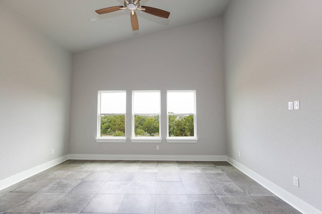 an empty room with three windows and a ceiling fan