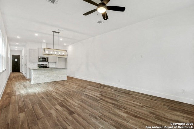 an empty living room with a kitchen and a ceiling fan
