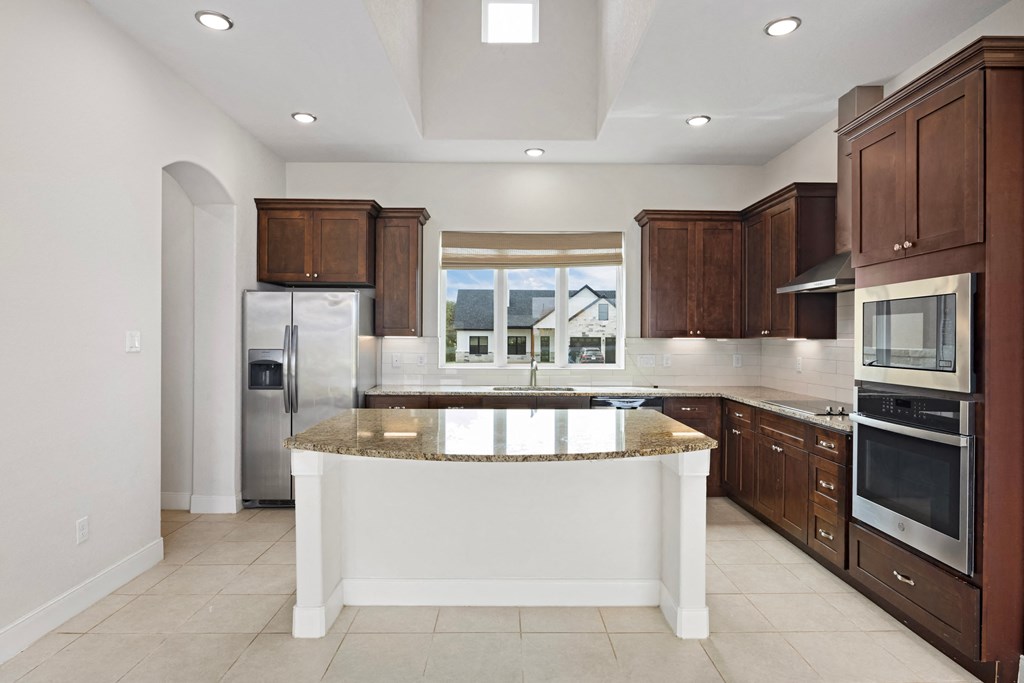 a large kitchen with brown cabinets and a marble counter top
