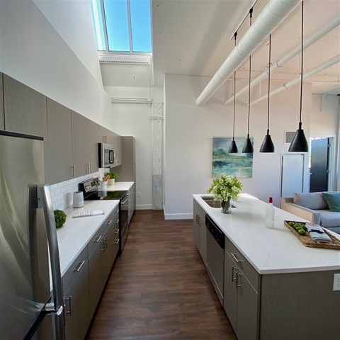 A modern kitchen with a refrigerator on the left and a dining area with a couch in the background.