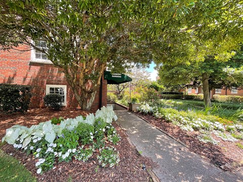 a sidewalk in front of a brick building with trees and flowers