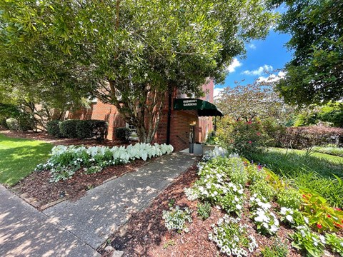 a sidewalk in front of a brick building with flowers and trees