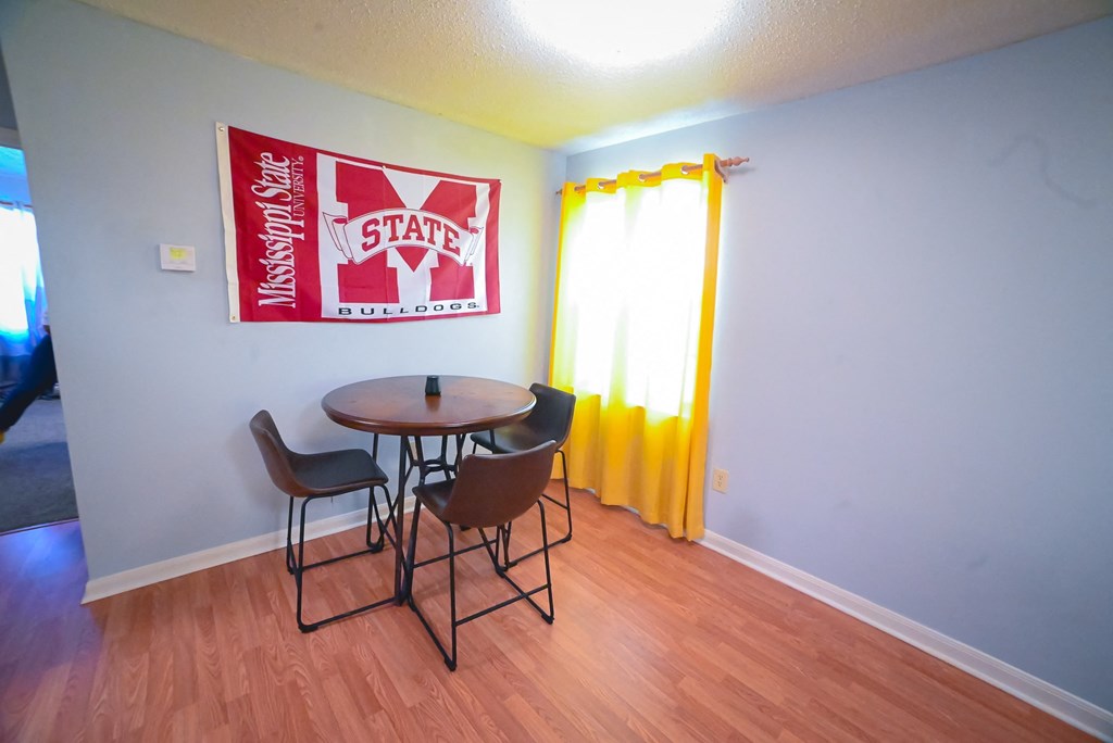 a dining room area with a table and chairs and a window with a yellow curtain