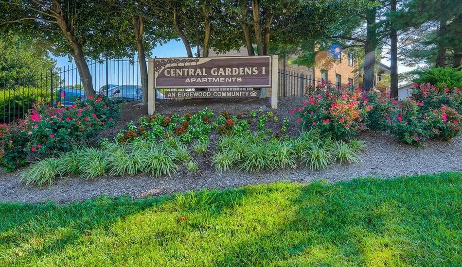 a park with flowers and a sign for central gardens apartments