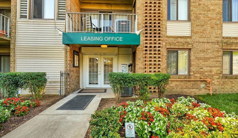 a building with a green leasing office sign in front of a garden