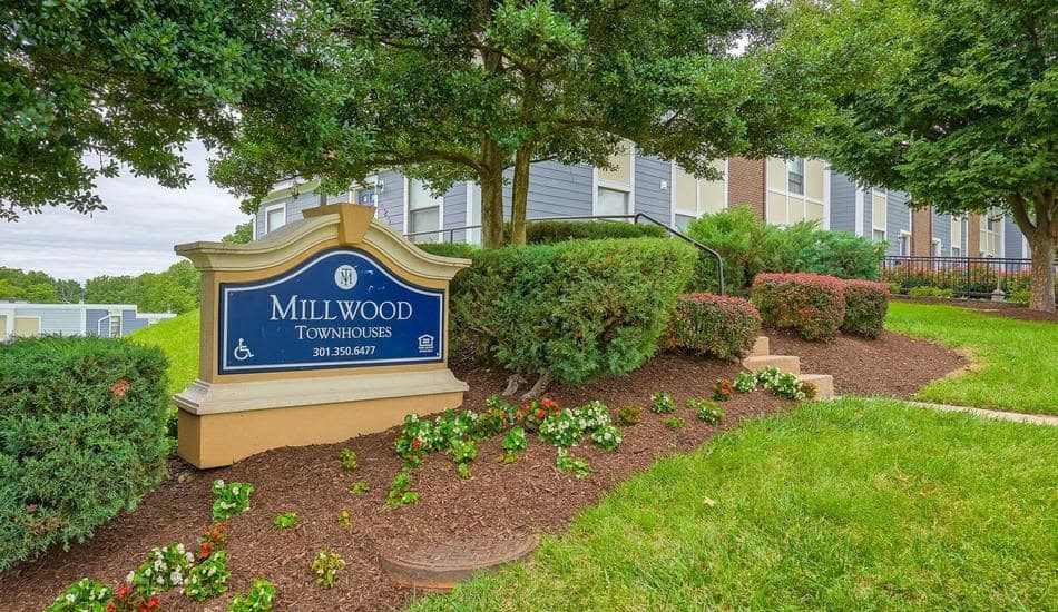a sign for millwood townhomes in front of trees and bushes