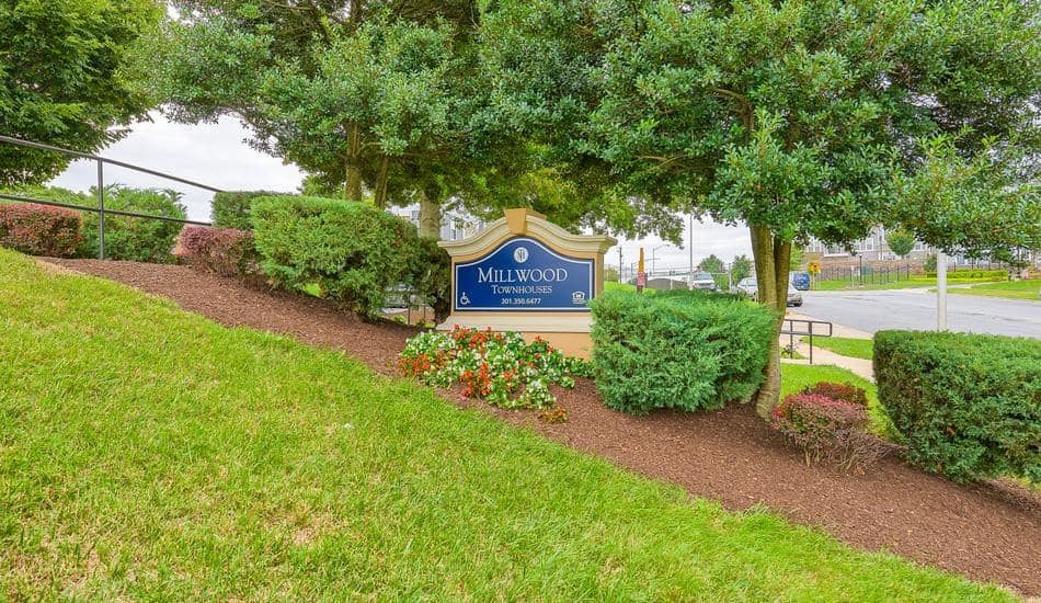 a sign in front of a park with trees and bushes
