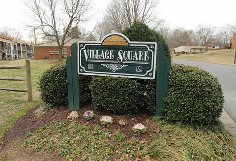 a sign for village square in front of some bushes