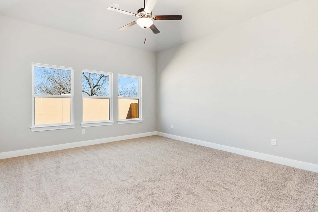 an empty living room with three windows and a ceiling fan
