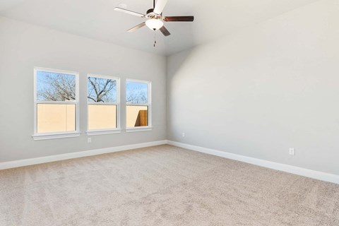 an empty living room with three windows and a ceiling fan