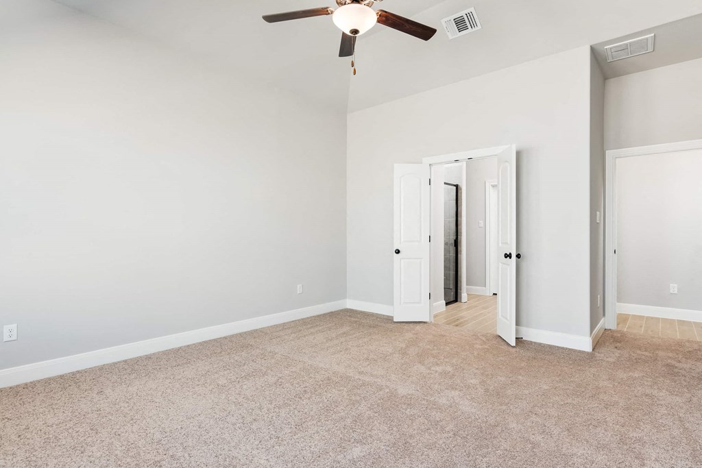 an empty living room with a ceiling fan and a door to a hallway