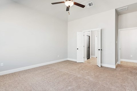 an empty living room with a ceiling fan and a door to a hallway