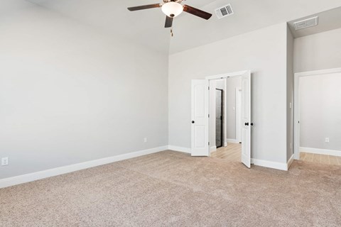 an empty living room with a ceiling fan and a door to a hallway
