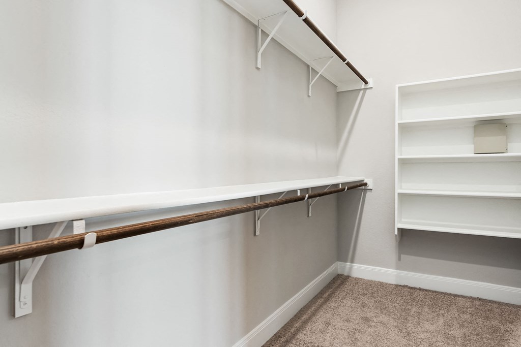 a walk in closet with white walls and shelves and a white shelf with hooks