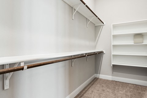 a walk in closet with white walls and shelves and a white shelf with hooks
