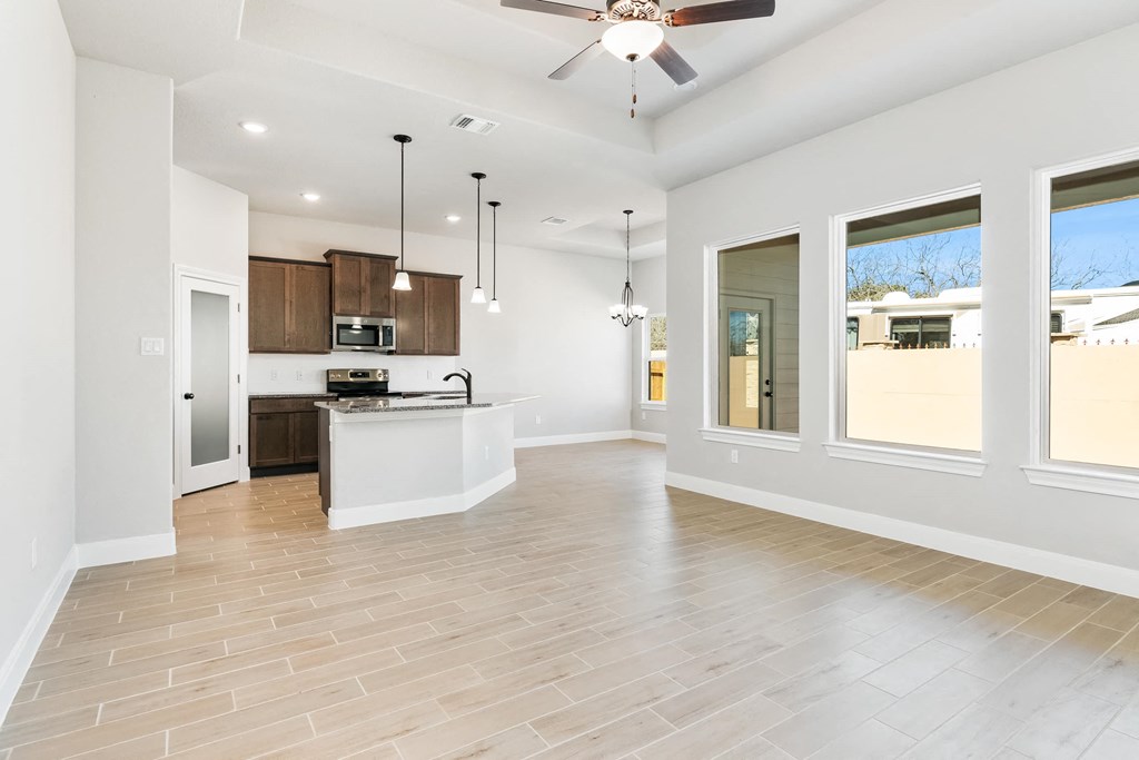 an empty living room with a kitchen and a ceiling fan