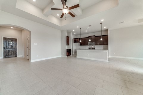 an empty living room with a ceiling fan and a kitchen