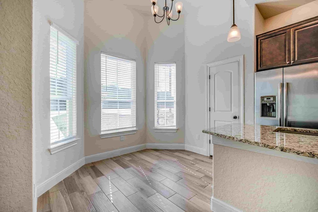 an empty living room with three windows and a kitchen
