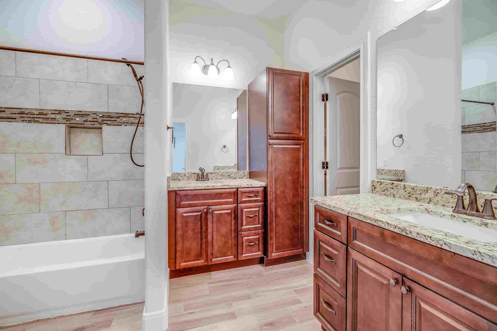 a bathroom with wooden cabinets and a tub and a sink and a shower