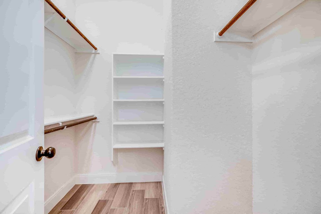 a small closet with shelves in a white room with wood floors