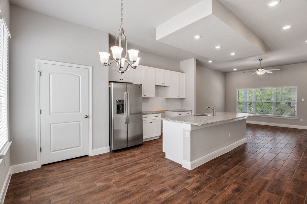 an open kitchen and living room with white cabinets and a stainless steel refrigerator