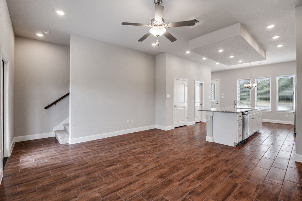 an empty living room with a ceiling fan and a kitchen