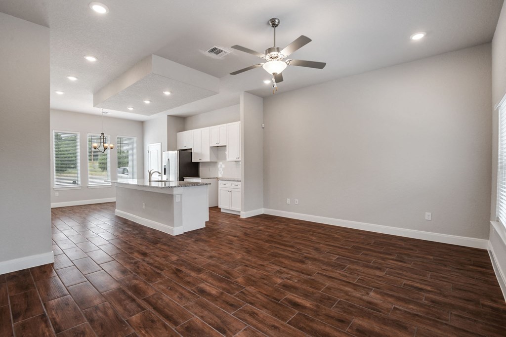 an empty living room with a ceiling fan and a kitchen