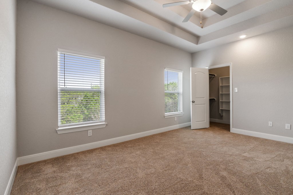 an empty living room with two windows and a ceiling fan