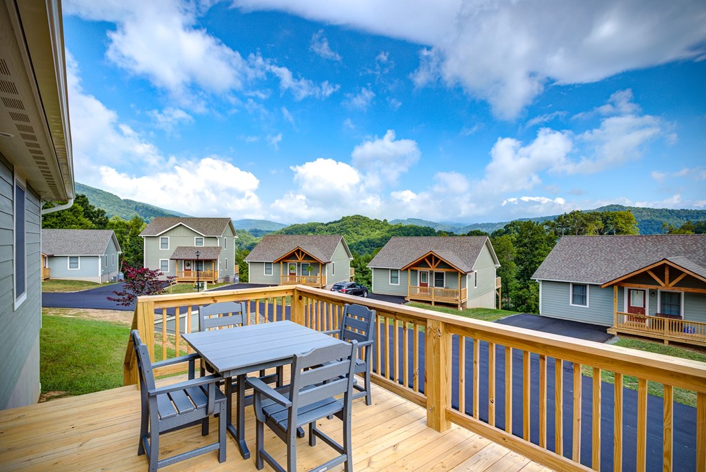 A wooden deck with a table and chairs overlooks a mountainous landscape.