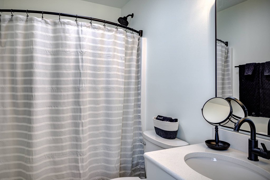 A bathroom with a white sink, a striped shower curtain, and a round mirror.
