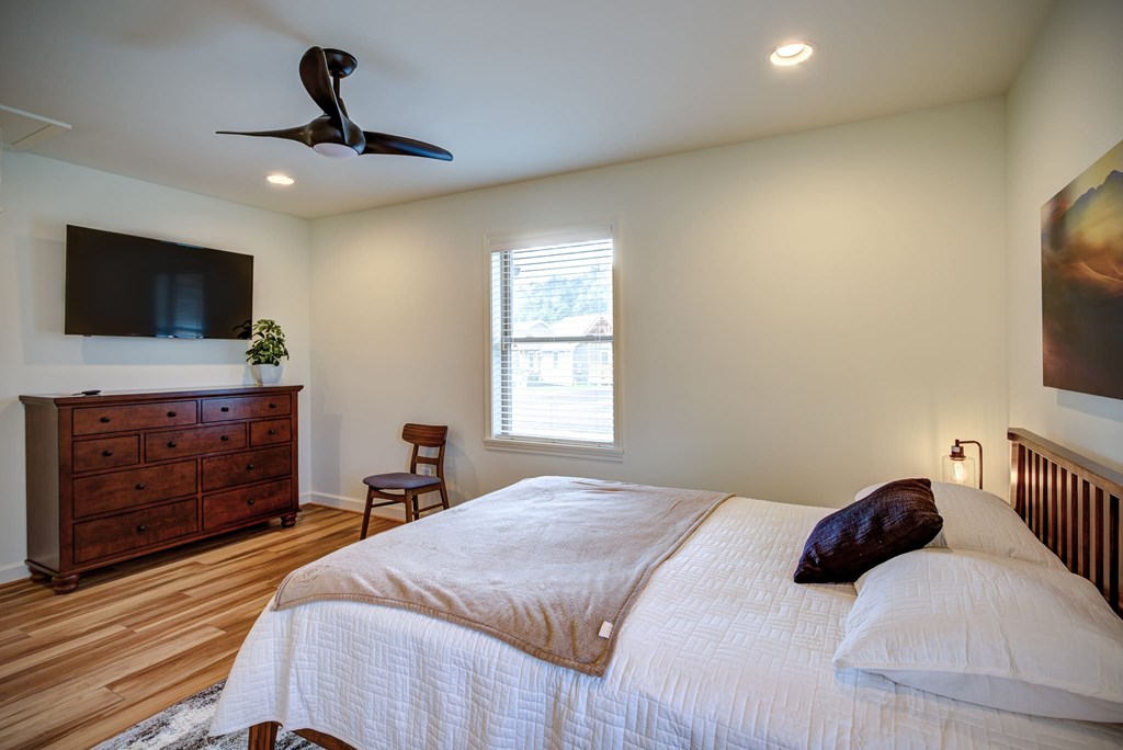 A bedroom with a bed, a dresser, a chair, a ceiling fan, and a window.