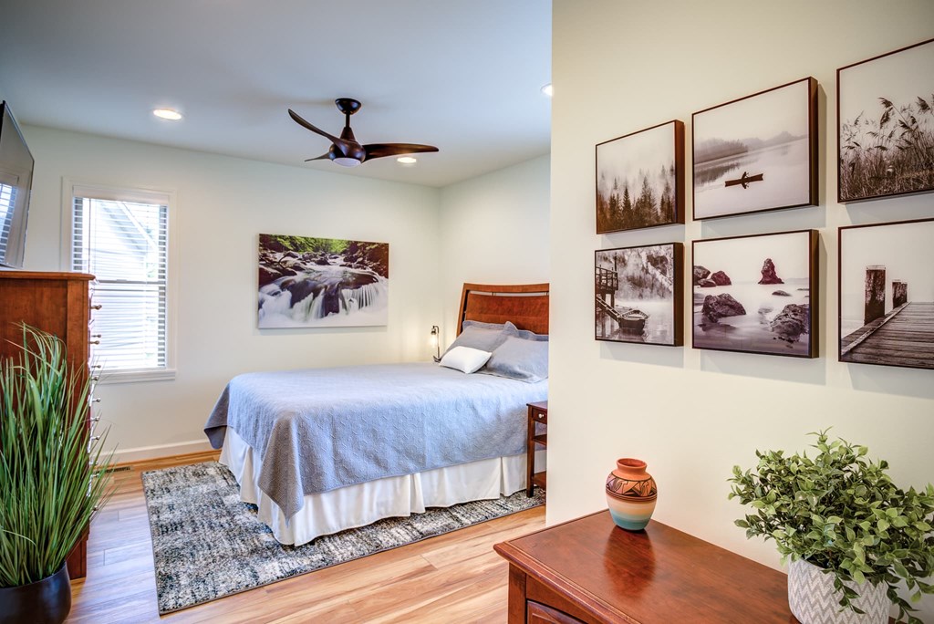 A bedroom with a bed, a ceiling fan, and pictures on the wall.