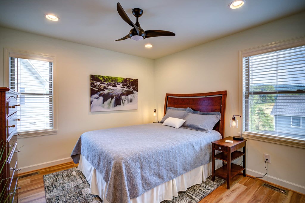 A bedroom with a bed, a ceiling fan, and a painting on the wall.