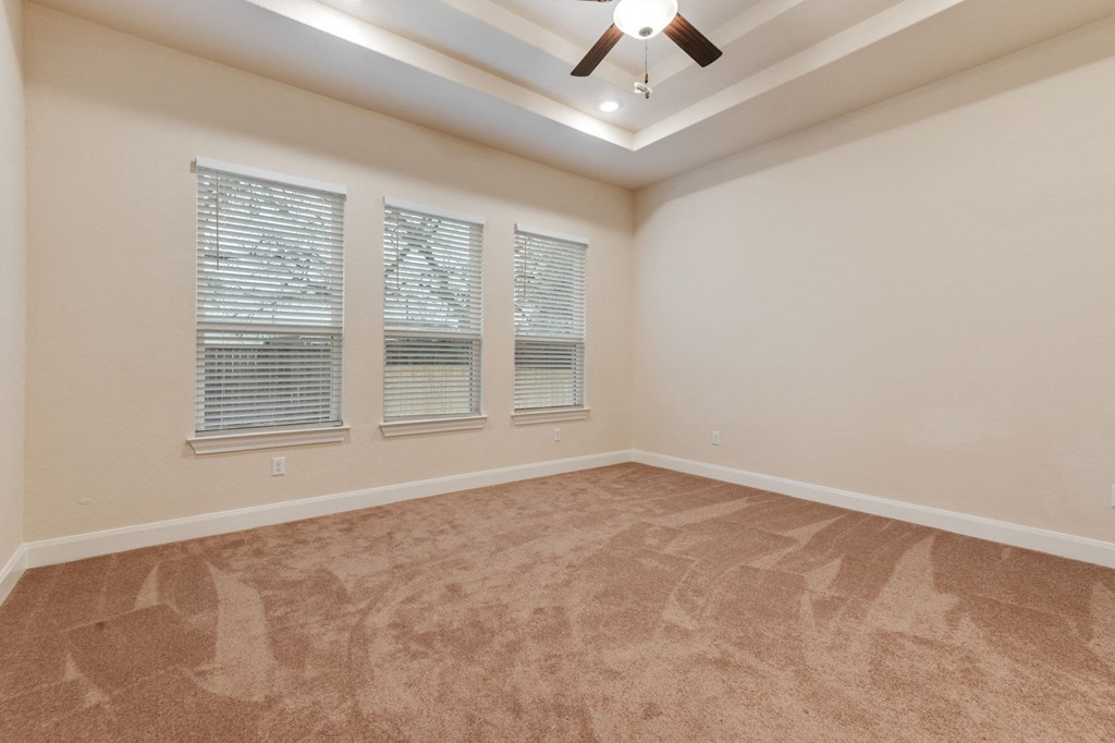 an empty living room with three windows and a ceiling fan