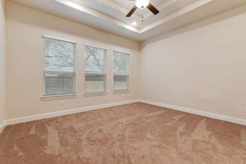an empty living room with three windows and a ceiling fan