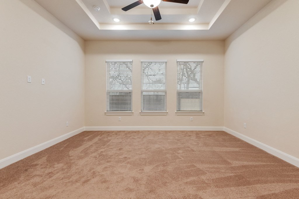 an empty living room with a ceiling fan and three windows