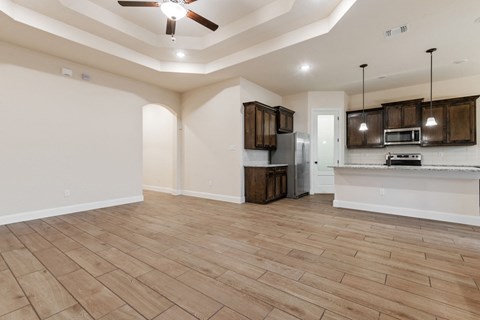 an empty living room with a kitchen and a ceiling fan