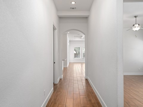 a long hallway with white walls and wood floors and a ceiling fan