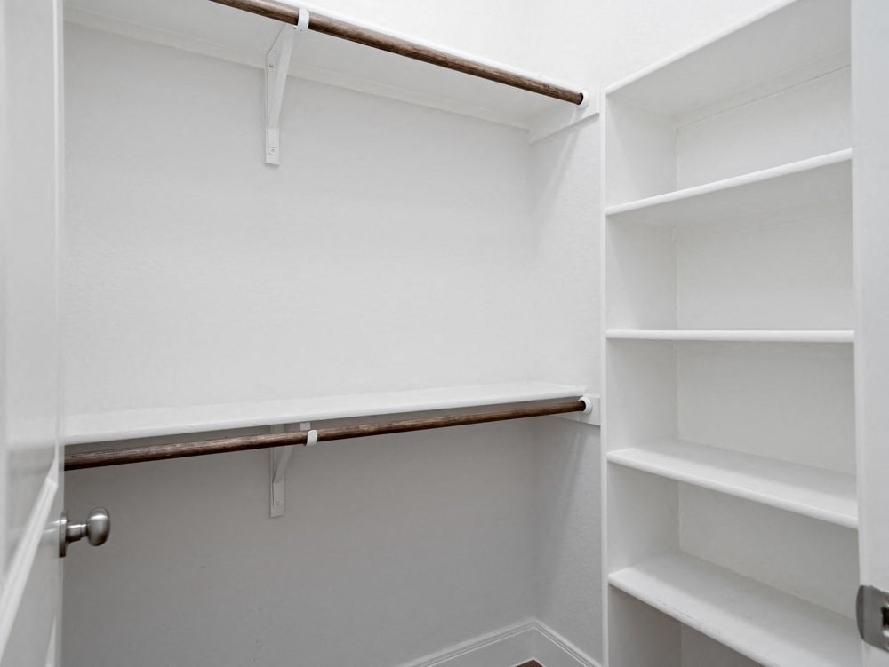 a walk in closet with white walls and shelves and a rail on the wall