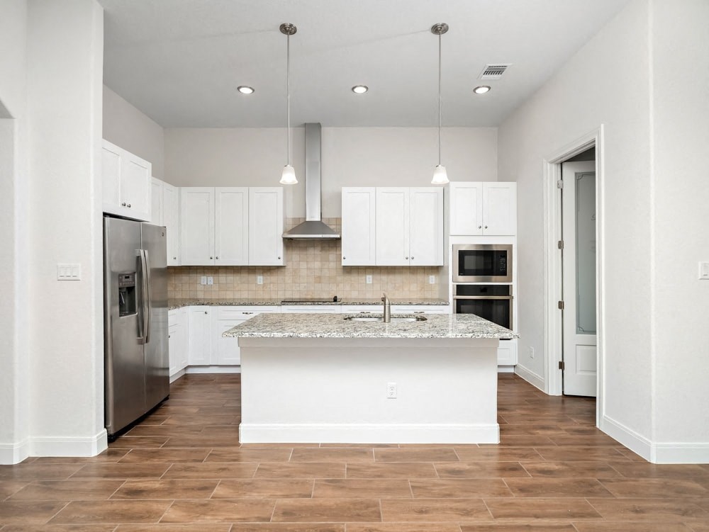 a white kitchen with a large island and stainless steel refrigerator