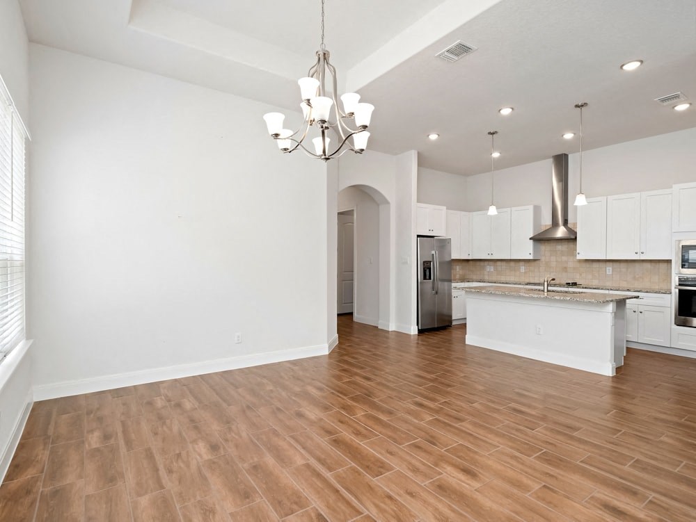 an empty living room with a kitchen and a chandelier