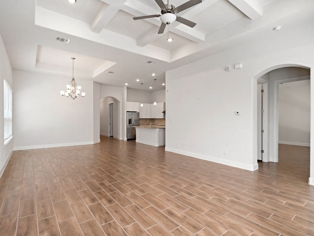 an empty living room with a ceiling fan and a kitchen