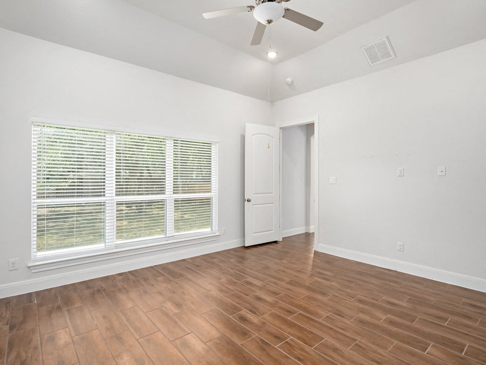 an empty living room with a large window and a ceiling fan